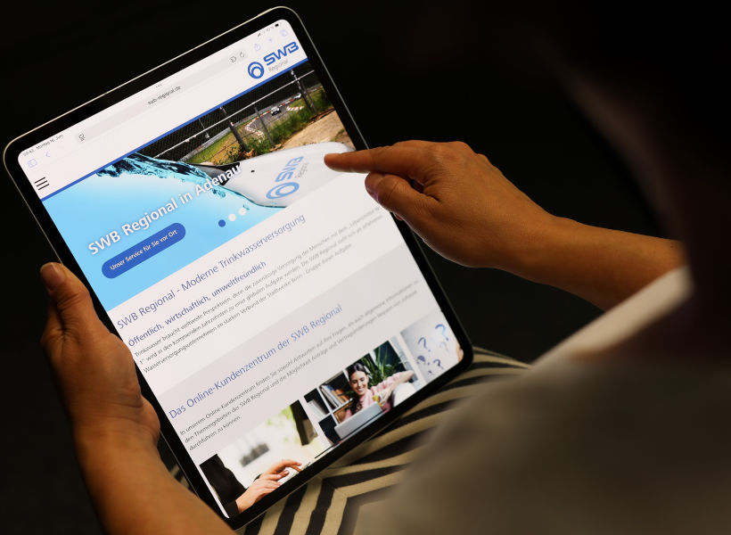 Eine sitzende Frau hält ein Ipad in den Händen. Auf diesem ist die neue Webseite der SWB Regional zu sehen.